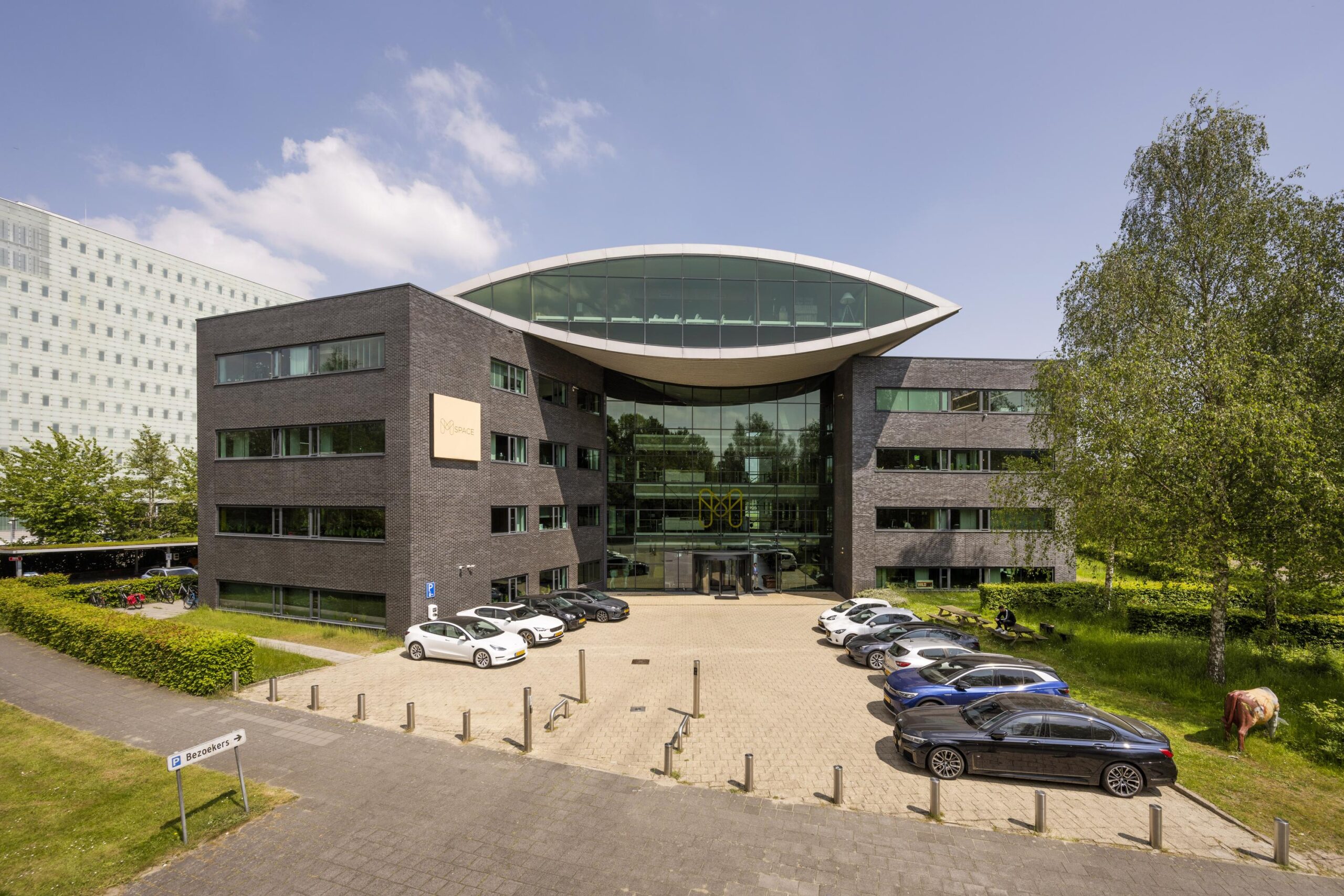 Modern kantoorgebouw aan de Prof. W.H. Keesomlaan met parkeerplaats en auto's op de voorgrond.